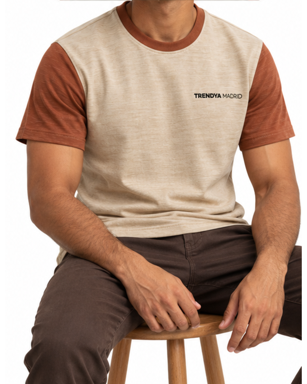 Camiseta de hombre beige arena con mangas terracota puesta, modelo sentado en un taburete