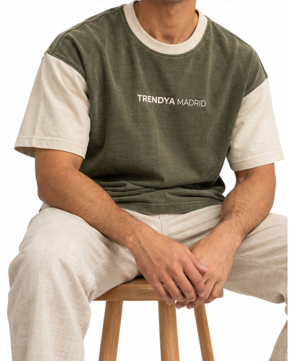 Camiseta holgada de hombre verde oliva con mangas crema puesta, modelo sentado en un taburete