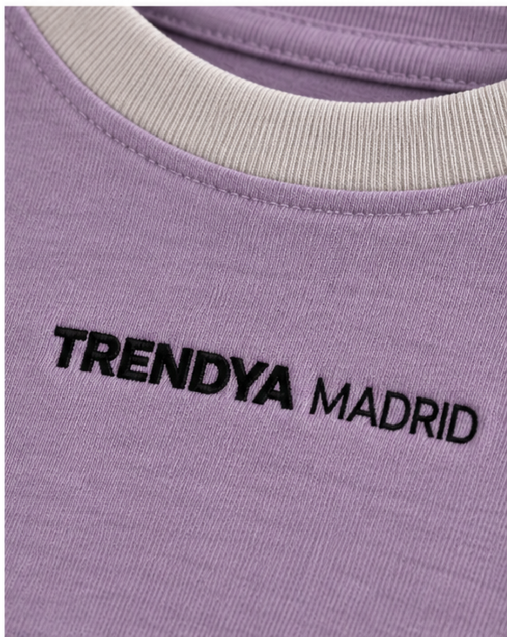 Detalle del cuello de canalé gris piedra y del logotipo Trendya Madrid bordado sobre el lavanda